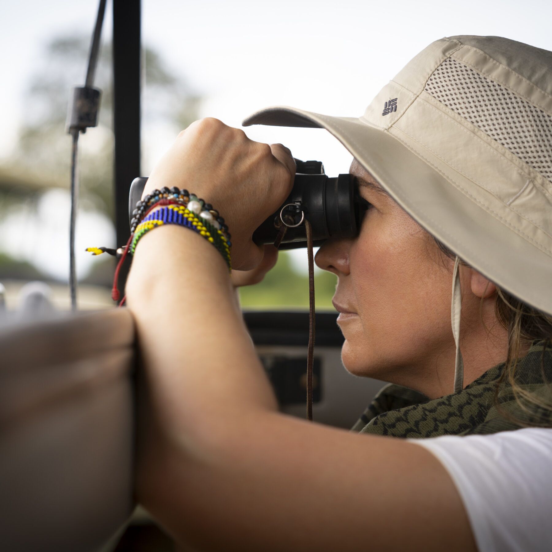 Woman with a hat and binoculars looking out from a car in Serengeti