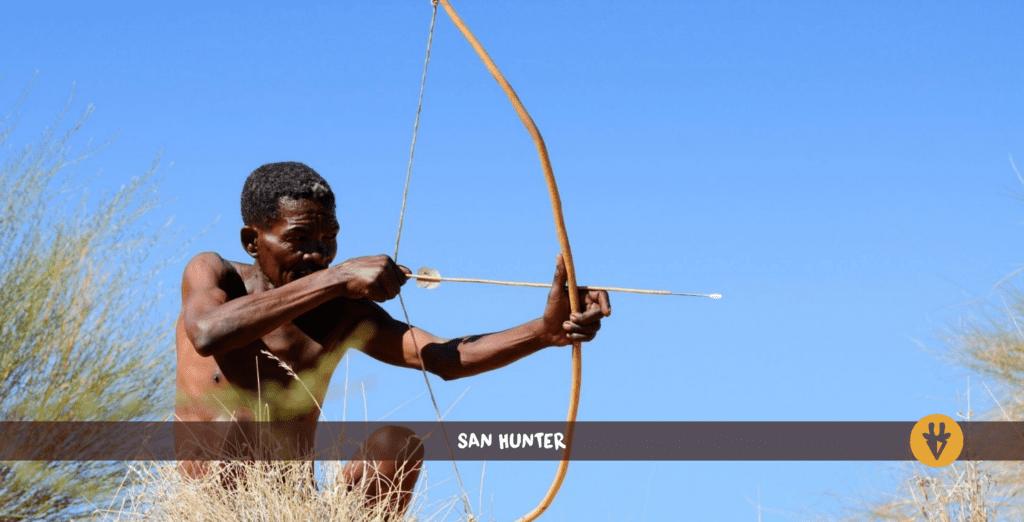 San Bushman with bow and arrow on a hill with some grass in front