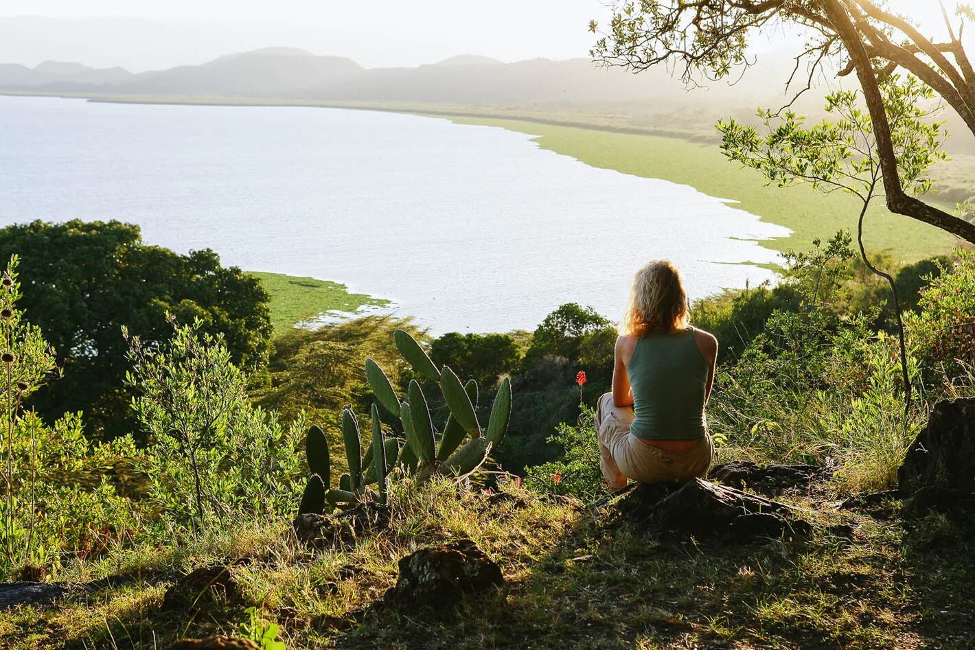 Woman sitting on a rock looking towards the green landscape and Lake Naivasha