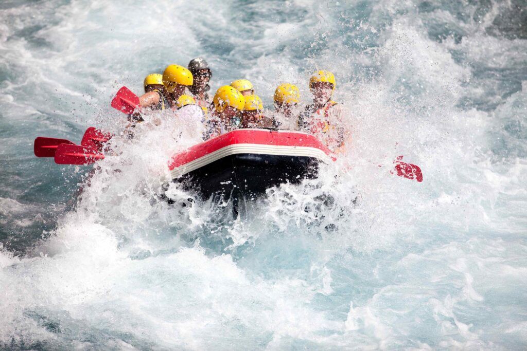 People with yellow helmets in raft going through rapids