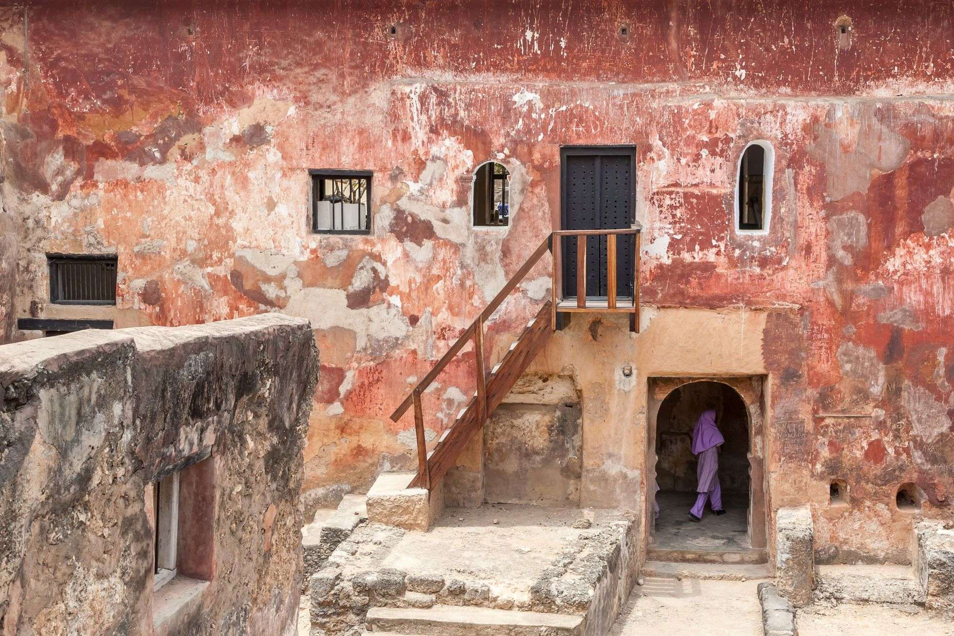 Ancient red building with wooden stairs and woman going into the building