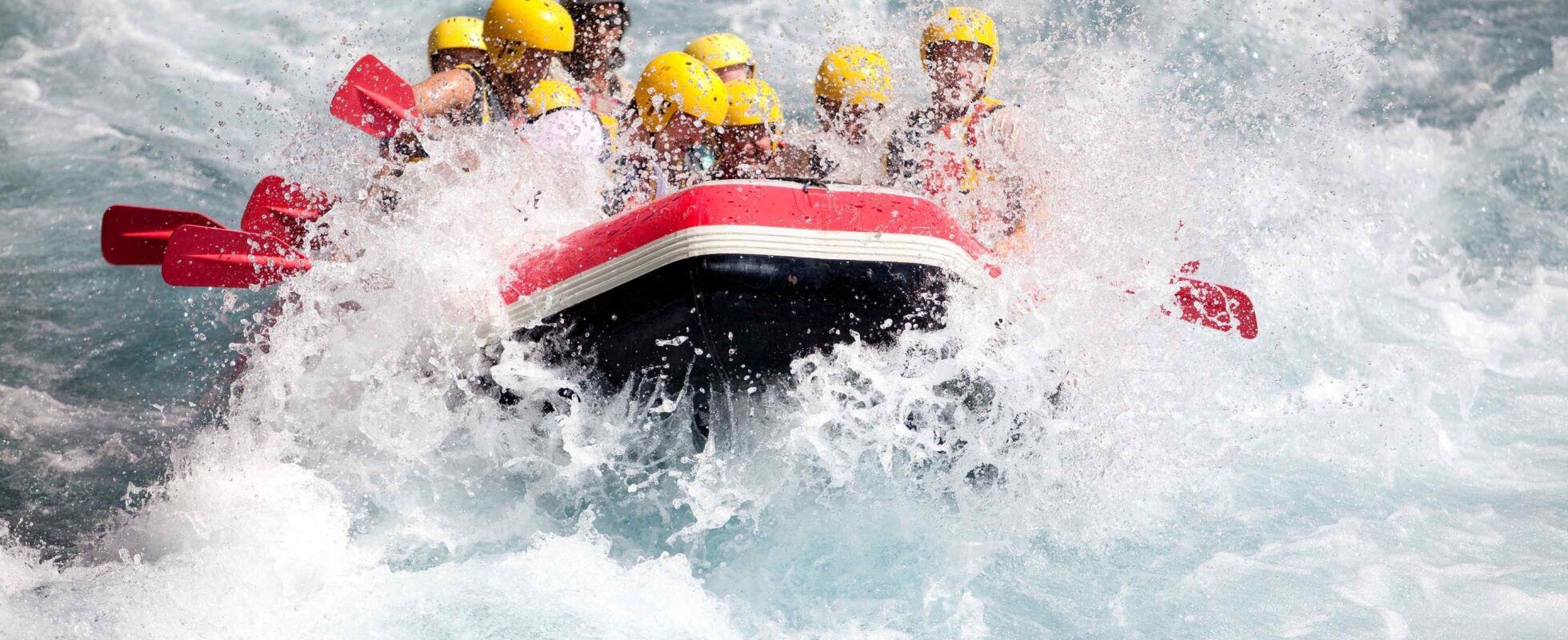 People with yellow helmets in raft going through rapids